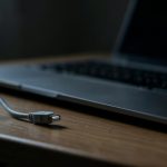 An unplugged cable beside a laptop with a dark screen on a desk
