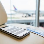 A smartphone and a boarding pass on an airport bench with a plane visible through the window