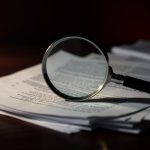 Magnifying glass over a stack of legal documents on a dark desk, checking a court PDF for searchable text