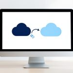 A desktop monitor showing two cloud icons with an arrow moving a file from one cloud to another, representing a Dropbox to OneDrive move
