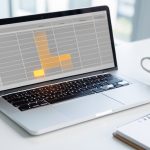 A laptop showing an abstract spreadsheet grid with one cluster of cells glowing amber like a spill warning