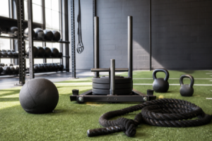 Functional-training gym equipment on turf, including a sled, kettlebells, a medicine ball, and a battle rope