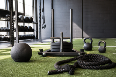Functional-training gym equipment on turf, including a sled, kettlebells, a medicine ball, and a battle rope