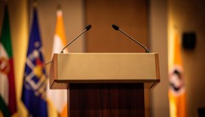 An empty conference lectern with microphones and blurred flags under warm lighting