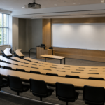 An empty university lecture hall with tiered seating and a blank whiteboard