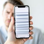 A hand holding an iPhone showing a news feed of repeated, near-identical story cards