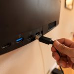 A hand plugging an HDMI cable into one of the ports on the back of a wall-mounted television