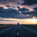 A long empty highway stretching to the horizon at dusk with a distant fuel tanker truck