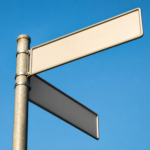 Blank street signs on a pole against a bright blue sky
