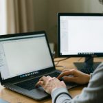 A person at a Windows laptop organizing files and folders with a second monitor on the desk