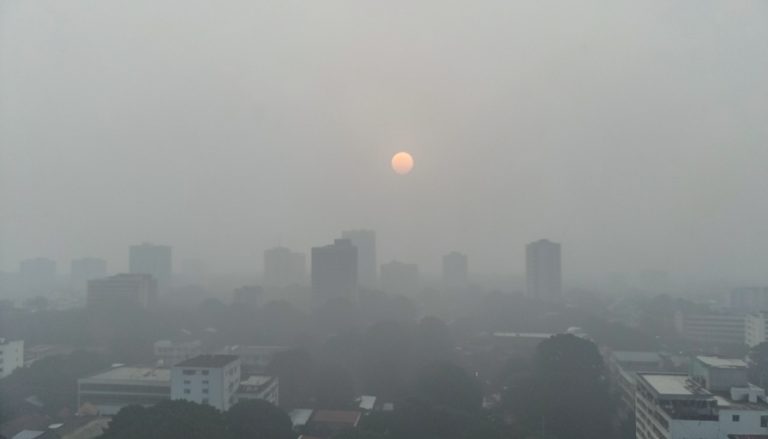 A Southeast Asian city skyline shrouded in thick grey haze at midday