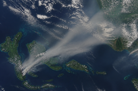 Aerial view of grey smoke plumes drifting from a green archipelago across the sea