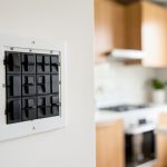 An electrical breaker panel on a wall with a modern kitchen and range blurred in the background