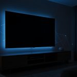 A wall-mounted smart TV glowing in a dark living room with faint network connection lines
