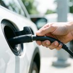A hand plugging a fast-charging connector into an electric car's charge port at a charging station