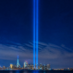 Two beams of light rising into the night sky over the New York City skyline