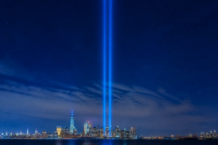 Two beams of light rising into the night sky over the New York City skyline