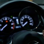A hand holding a magnifying glass up to a car's dashboard instrument cluster in low light