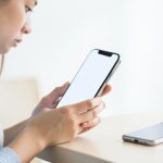 A person setting up a new smartphone with an older phone resting on the desk beside them