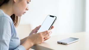 A person setting up a new smartphone with an older phone resting on the desk beside them