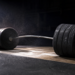 A heavily loaded barbell bending under stacked weight plates on a lifting platform with chalk dust in the air