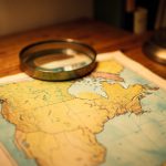 A vintage paper map of North America under a magnifying glass on a wooden desk