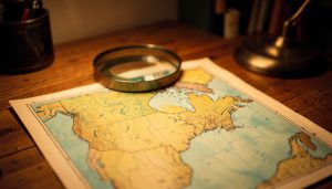 A vintage paper map of North America under a magnifying glass on a wooden desk