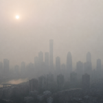 A city skyline shrouded in thick grey haze with a dim hazy sun