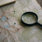 A topographic map on a table with a magnifying glass and small marker pins