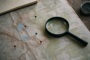A topographic map on a table with a magnifying glass and small marker pins