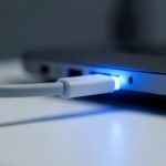 A USB-C cable plugged into the side port of a laptop with a soft blue power glow around the connector